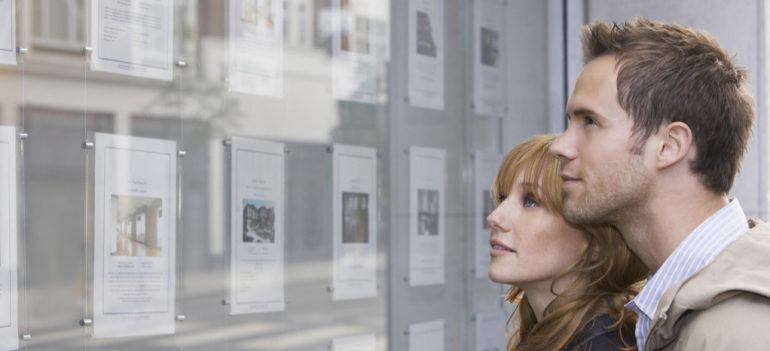 A couple looking at homes for sale in the window of an estate agent.